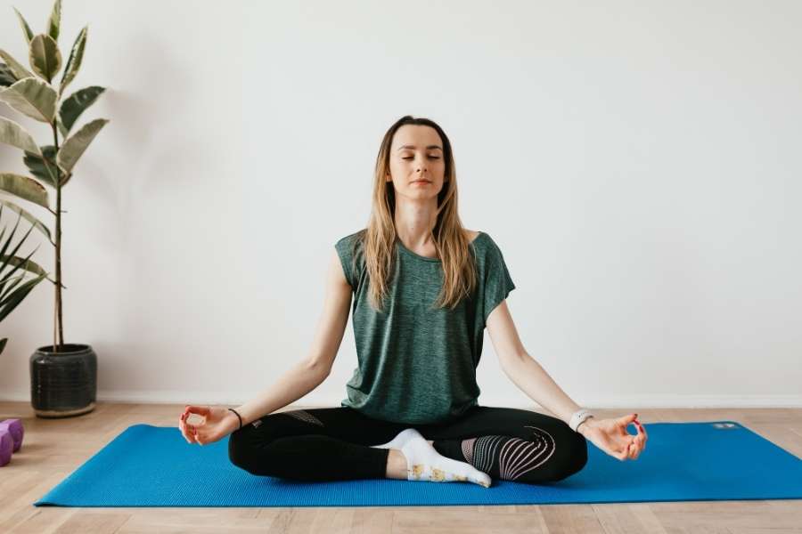 Une femme assise en tailleur sur un tapis pratique la méditation pour explorer les bienfaits insoupçonnés du yoga.