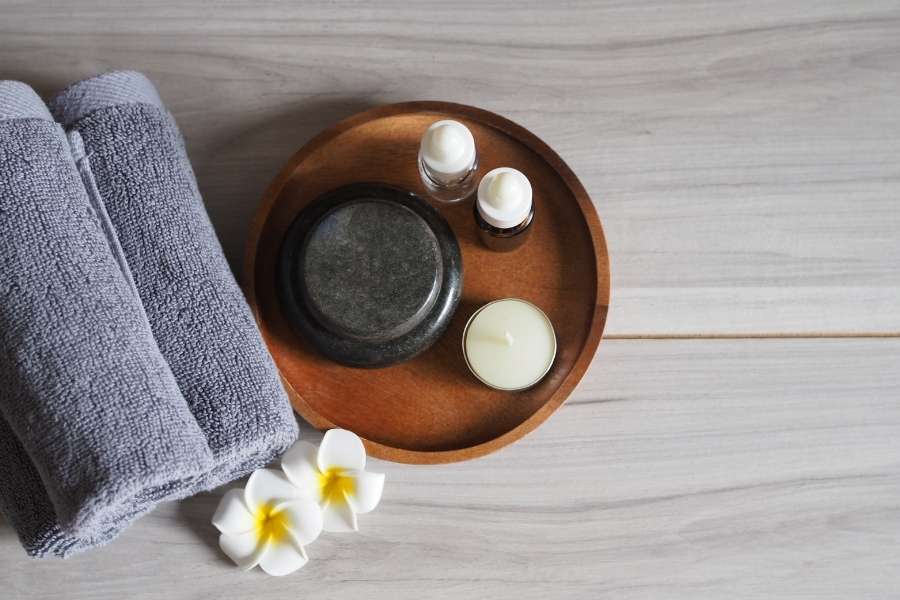 Alt text Un plateau de spa en bois avec des serviettes grises et des fleurs de frangipanier sur une table en bois clair.