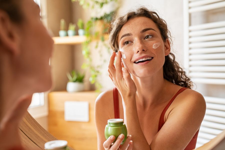 Femme souriante utilisant une crème fluide pour hydrater sa peau mixte sans la faire briller en cours de journée.   